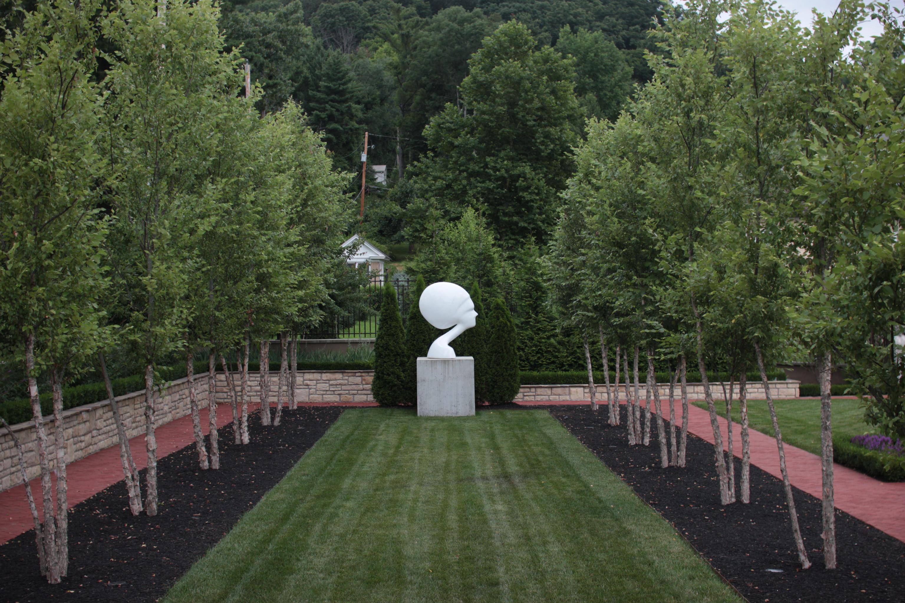 photo of a head sculpture at the end of a strip of grass, between two rows of trees